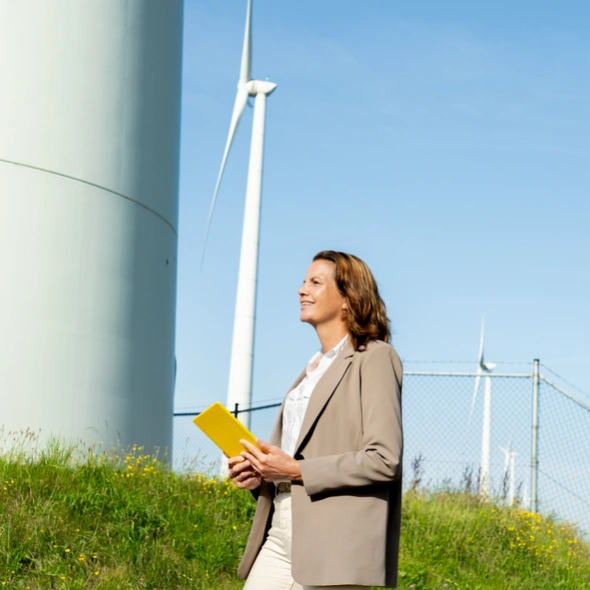 Kenonz collega met gele Ipad in haar handen kijkt voor zich uit met windmolens op de achtergrond.