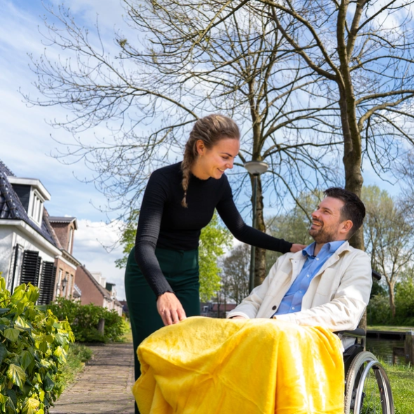 Kenonz collega die buiten zorgt voor man in rolstoel met geel kleed.