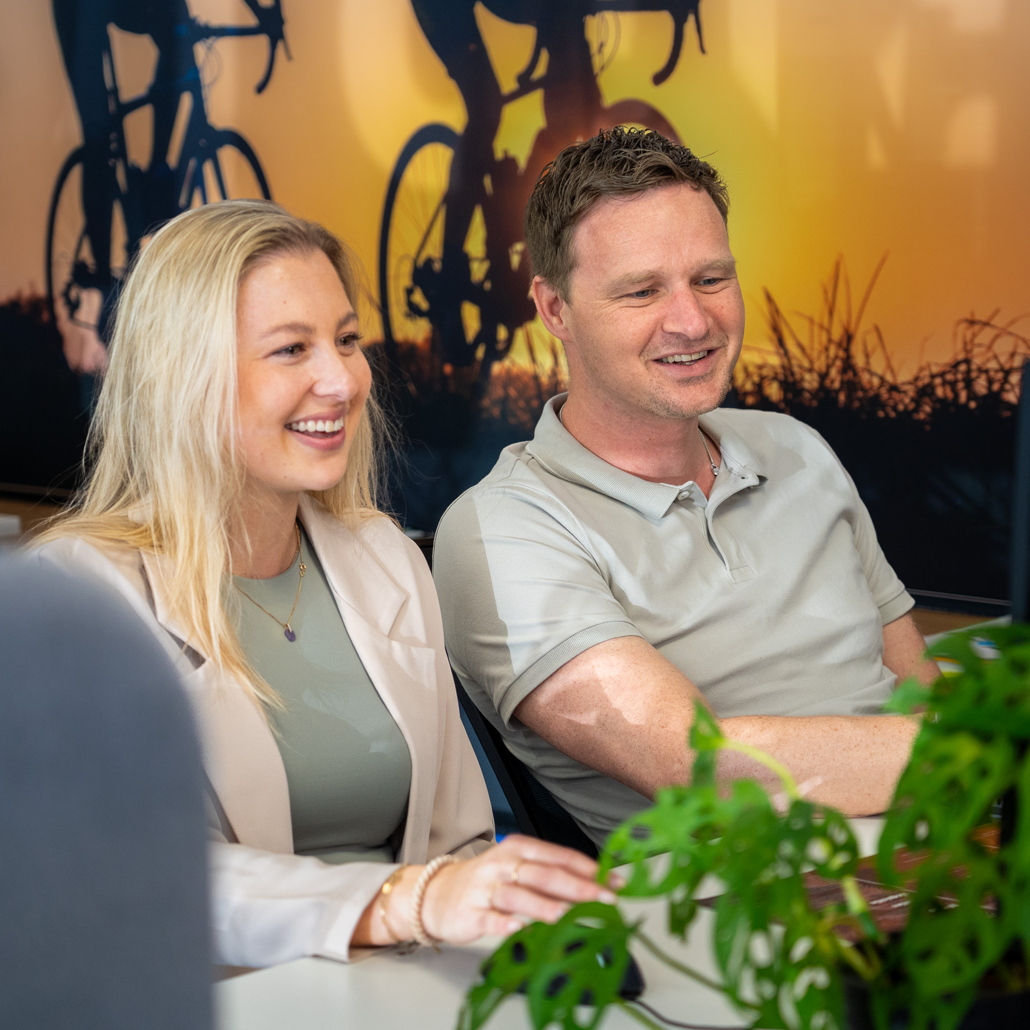 Twee Kenonz collega's lachend samen achter hun bureau, kijkend naar het beeldscherm.