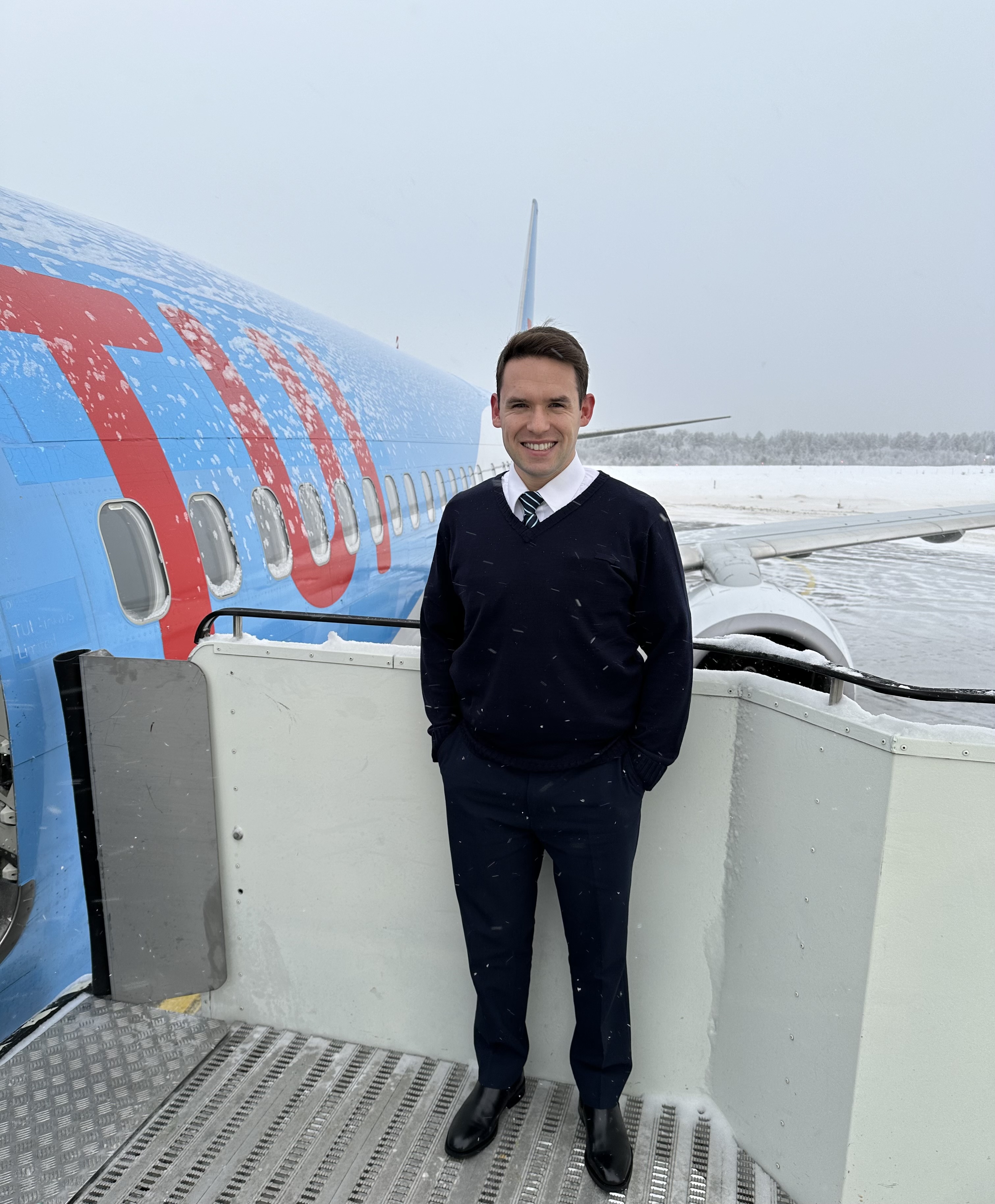 A male MPL Cadet stands at the doors of a TUI aircraft in a snowy airport landscape.