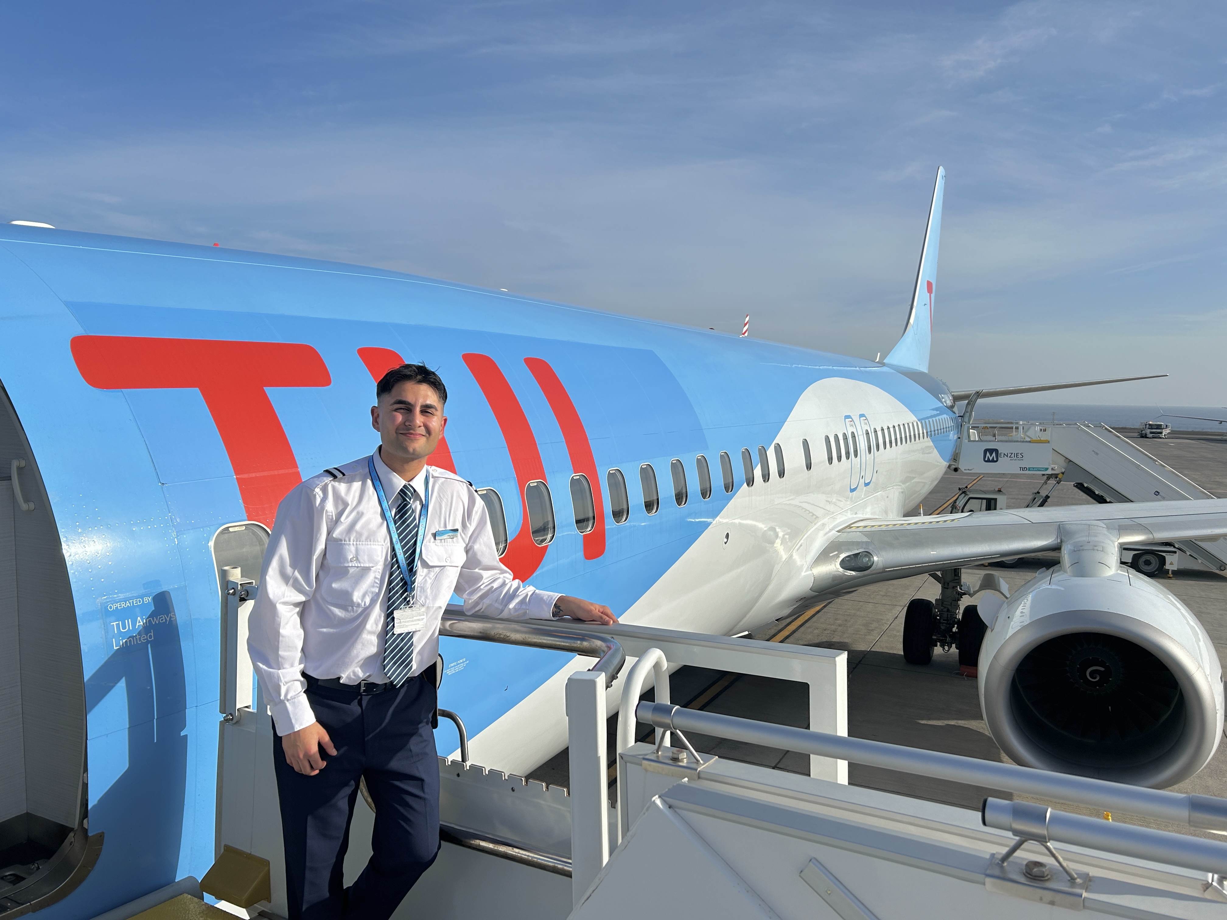 A male MPL Cadet Pilot stands smiling at a TUI aircraft with a blue sky background.