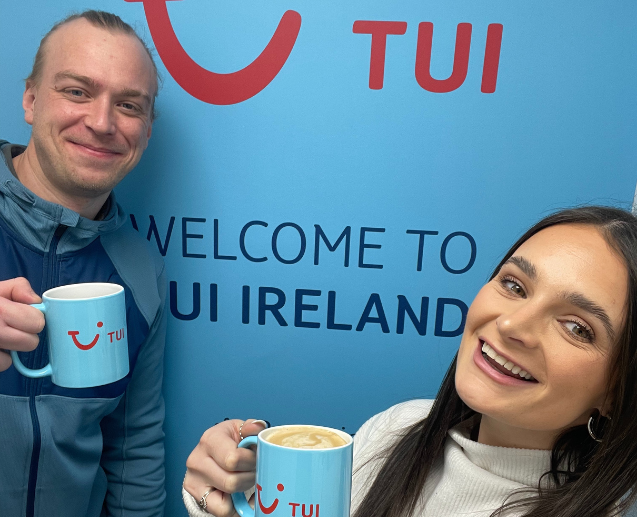 A male and a female standing in front of a sign that says 'Welcome to TUI Ireland' holding blue mugs with TUI on them.