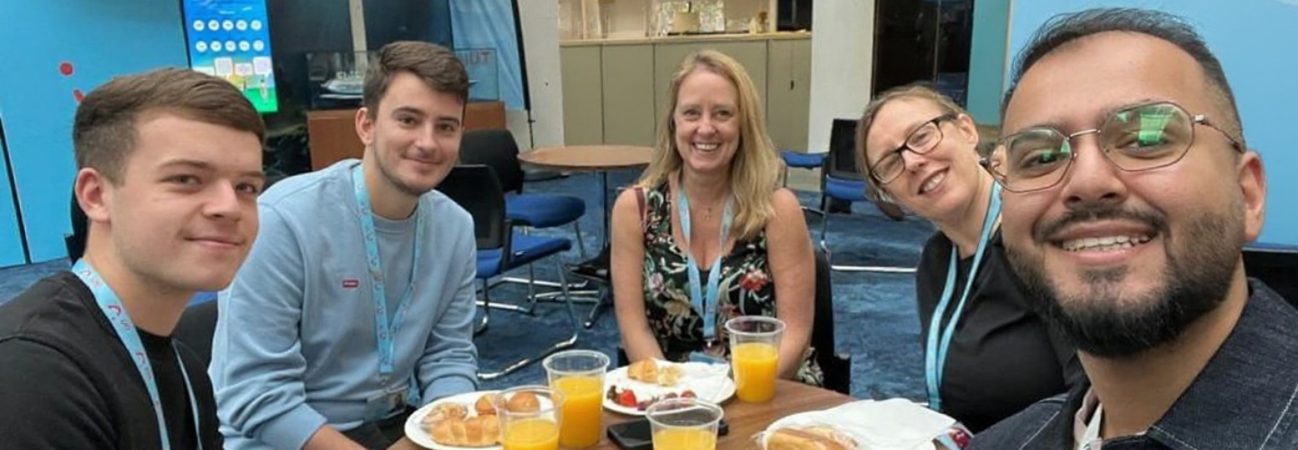 A group of five people smiling at a table with plates of food and glasses of orange juice.