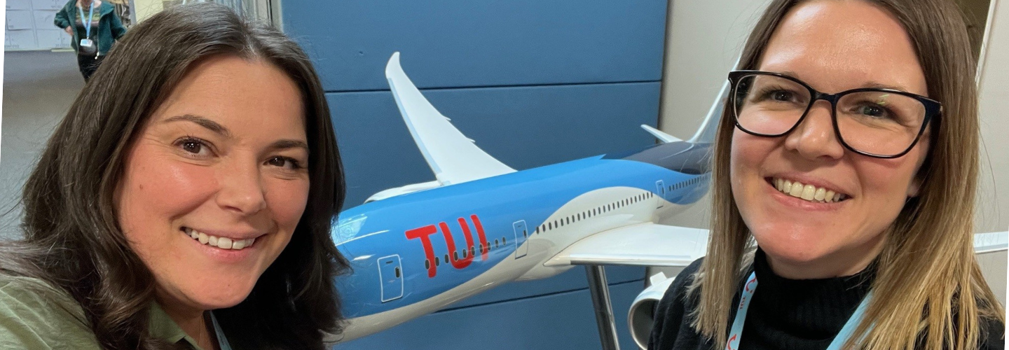 Two female colleagues smiling in front of a model TUI plane.