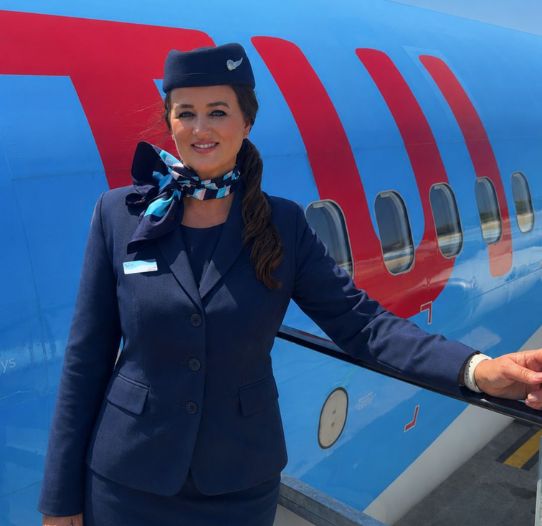 A TUI Cabin Crew member stands in uniform at a TUI aircraft door