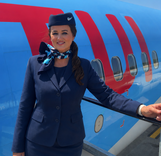 A TUI Cabin Crew member stands in uniform at a TUI aircraft door