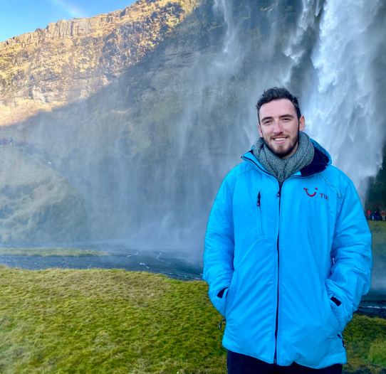 A TUI colleague stands in a TUI jacket in Iceland next to a waterfall
