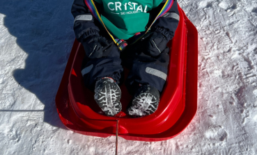 A young Crystal Ski guest wears a Crystal Ski bib on a sledge