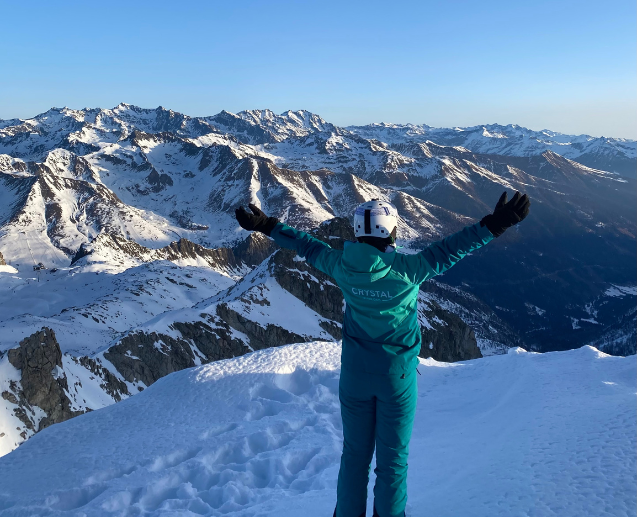 A Crystal Ski colleague stands with their back to the camera in front of a snowy mountain landscape