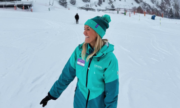 A Crystal Ski colleague wearing uniform and a bobble hat laughs in the snow