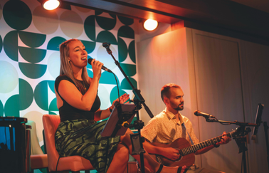 A woman sings and a man sat next to her plays guitar onboard a cruise ship.
