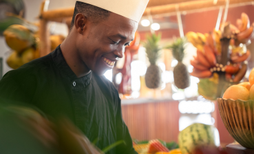 A chef stands around fruit and vegetable in The Mora