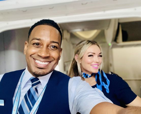 Two flight attendants, a man and a woman, taking a selfie on board a TUI plane, smiling to the camera.