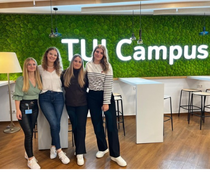 Eine Gruppe junger Frauen steht vor einer Moßwand mit dem leuchtenden Schriftzug "TUI Campus"