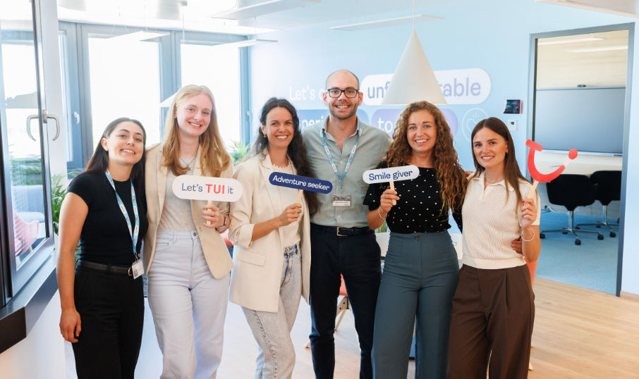 A group of young people smiling outdoors during a team moment.