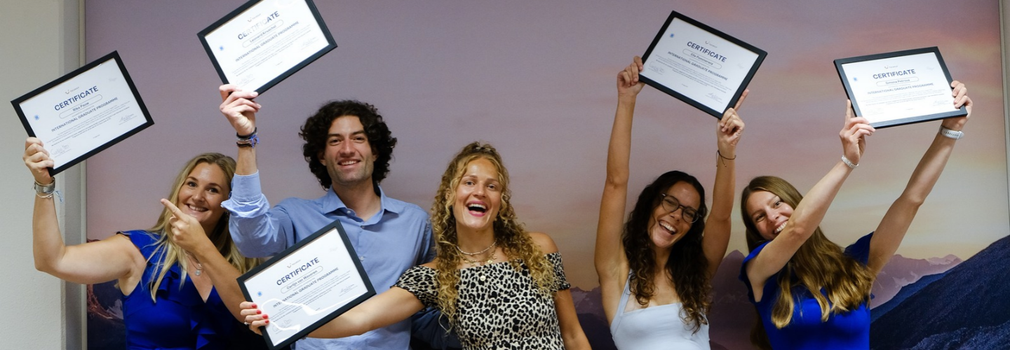 A group of three people smiling taking a selfie, in front of a blue wall with a red TUI logo, holding props that say 'Let's TUI it' and 'class of 2025'.