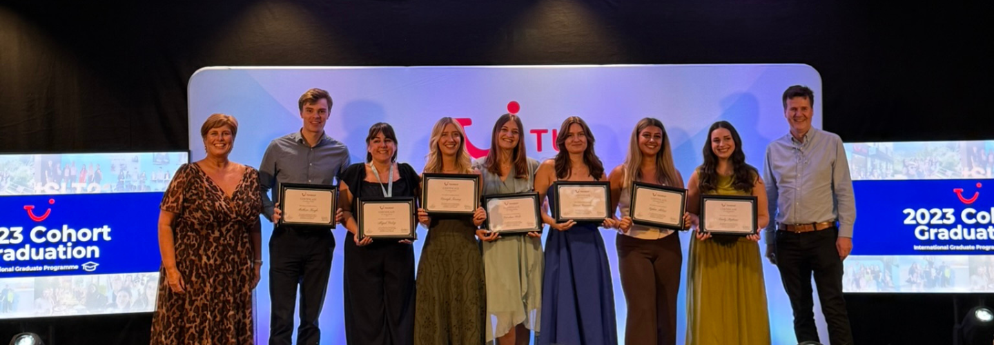 A group of 9 people stand on stage smiling with certificates.