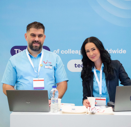 Two TUI colleagues stand smiling at a TUI booth at a job fair