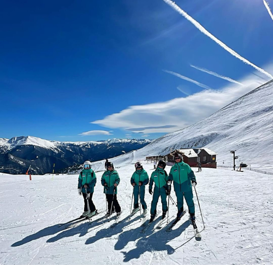 5 Crystal Ski colleagues stand on skis on a snowy mountain with a blue sky background