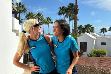 Two girls smiling at each other in front of palm trees