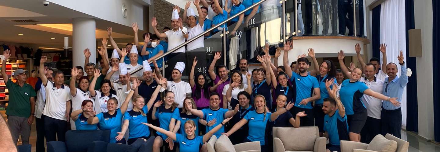 Large group of TUI Blue colleagues, ranging from Reps to Chefs, pose together on a hotel staircase.