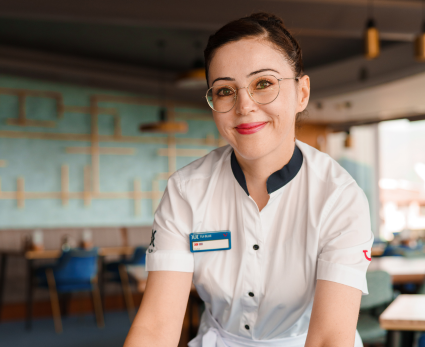 A female Food and Beverage colleague smiles at the camera in a restaurant setting.