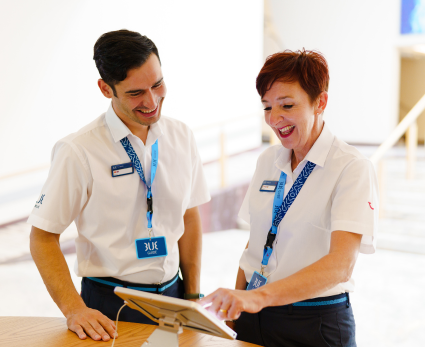 A male and female TUI BLUE colleague stand over a hotel iPad smiling.