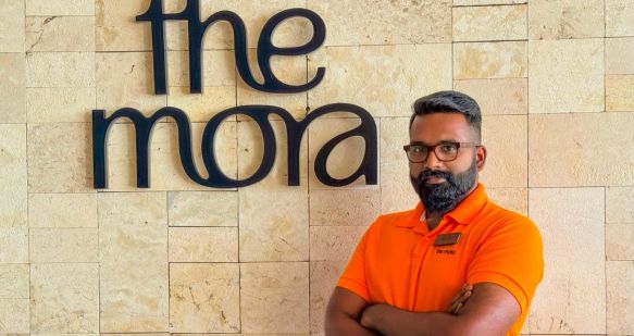 A The Mora colleague stands in uniform alongside a The Mora sign