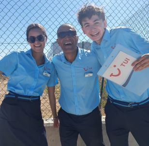 Three TUI Airport Reps stand together smiling at the airport holding a TUI clipboard
