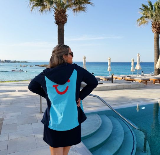 A TUI Rep stands in front of blue skies and palm trees at a hotel pool.