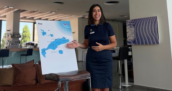 A TUI Rep stands in a hotel alongside a board with a map of Kos