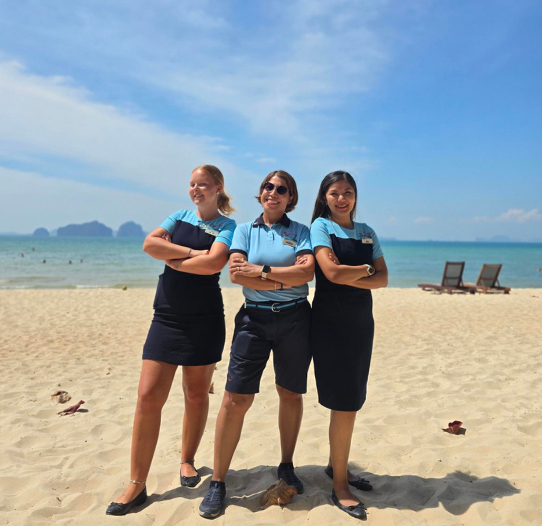 Three colleagues stand on a beach in Thailand