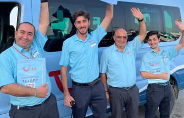Four TUI colleagues wave next to a transfer bus at Antalya Airport