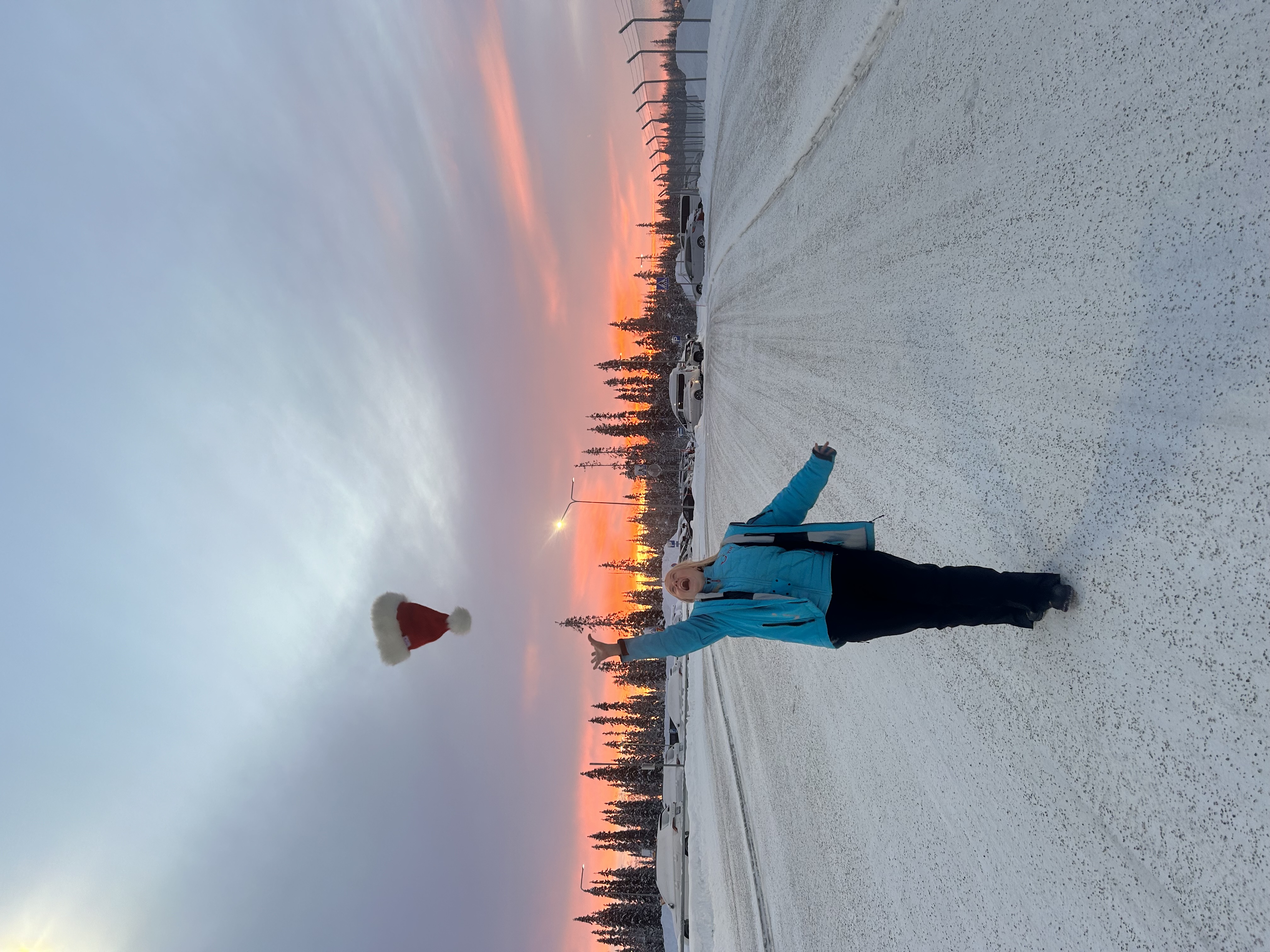 Person standing in snowy landscape at sunset, throwing a Christmas hat into the air.