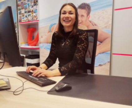 A woman is sitting at her desk in a TUI Retail store smiling in the Camera