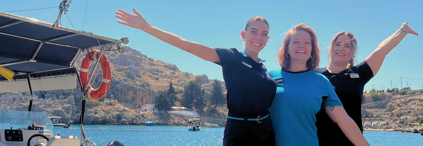 Three TUI Greece colleagues stand in front of a seaside landscape in Rhodes, Greece.