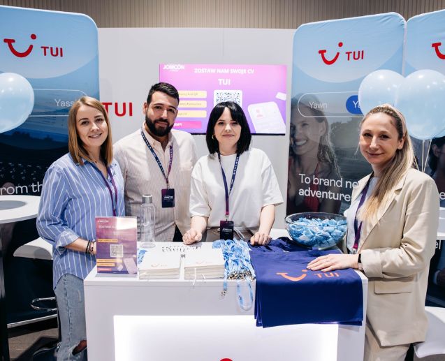 Four TUI Poland colleagues stand at a job fair alongside TUI stands and merchandise.