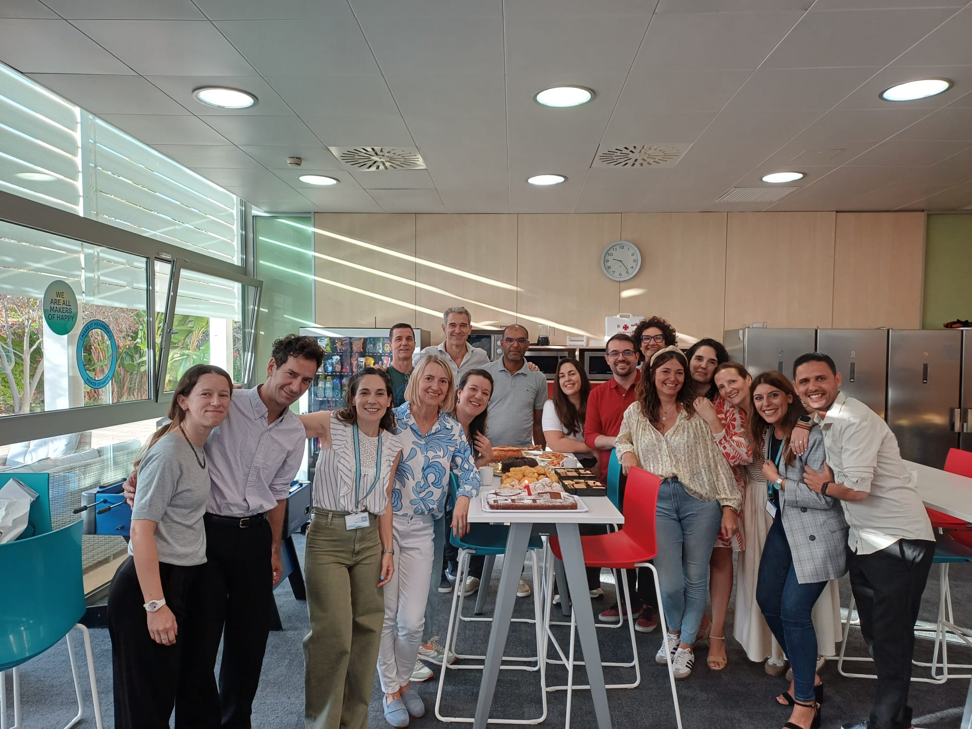 A group of male and female coworkers gathered around lunch table they are smiling.