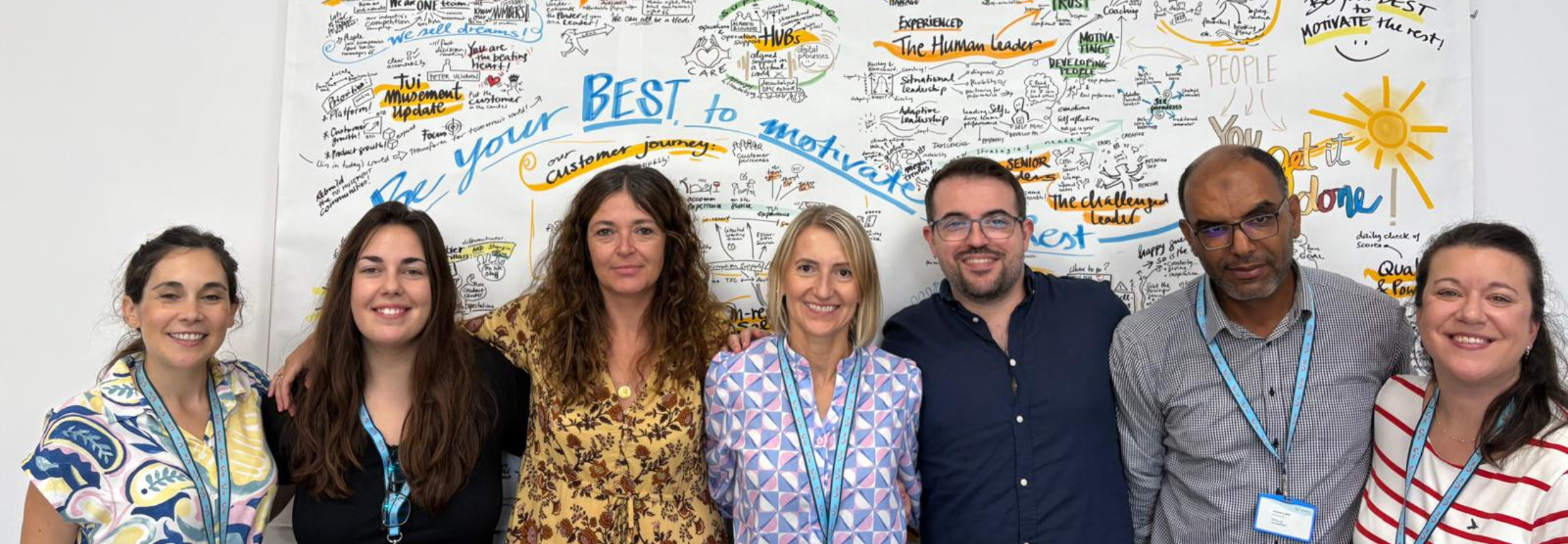 A group of happy smiling people stand in front of a wall that has drawing on it