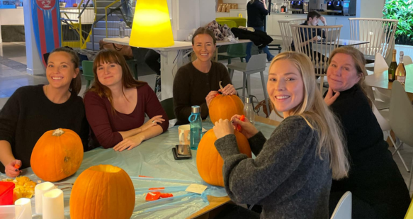 Female TUI Sweden colleagues sit at a table smiling at Halloween, carving pumpkins.