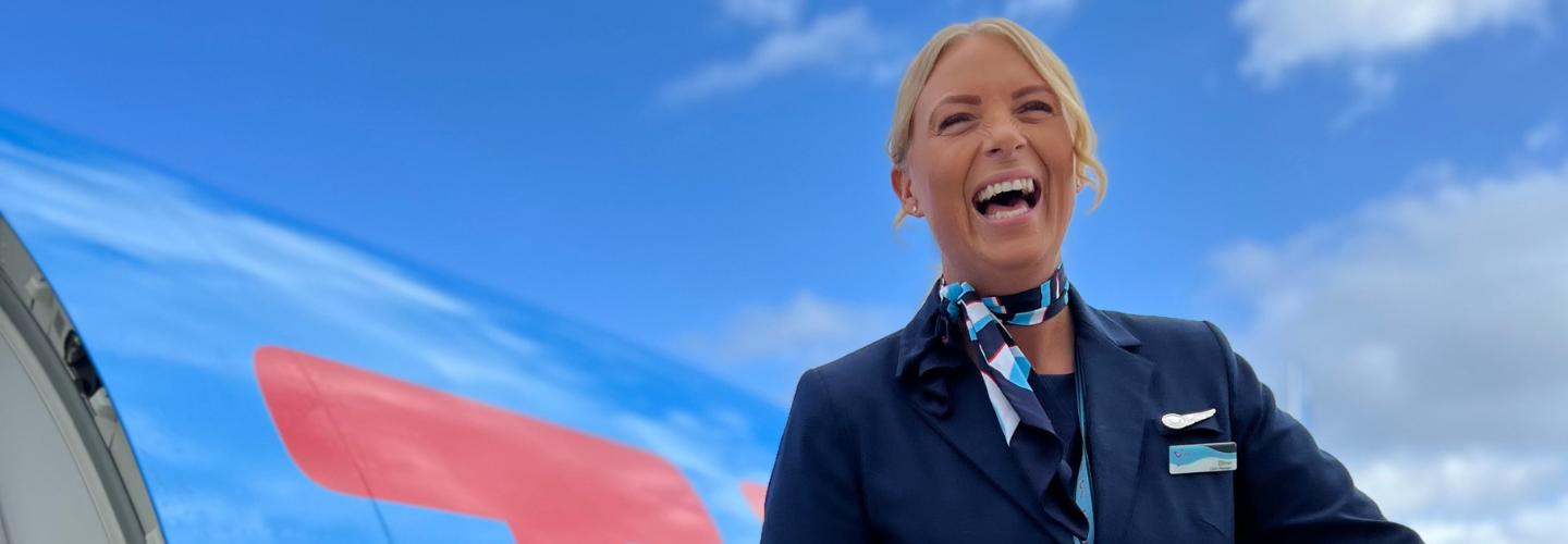 Female TUI fly Nordic Cabin Crew colleague laughs in front of an aircraft at Arlanda Airport