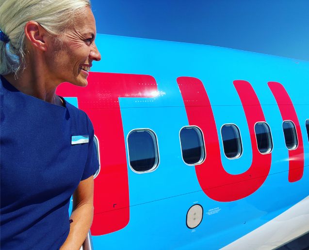 A TUI Sweden Cabin Crew colleague stands in front of a TUI aircraft smiling.
