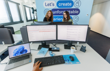 A Birds Eye view of a TUI colleagues desktop set up, with two colleagues conversing in the background together