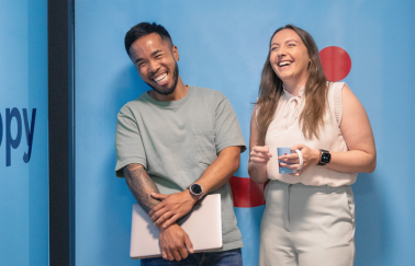 TUI colleagues stand laughing together in front of a blue wall background