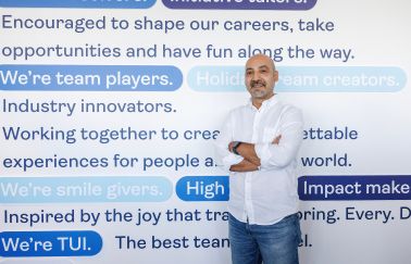 A TUI colleague stands smiling with a TUI branded background with employer branding slogans