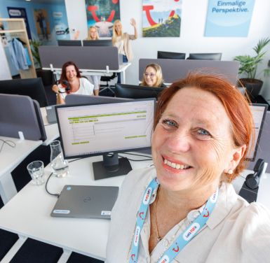 A group of TUI colleagues take a selfie in a TUI office surrounded by desks and monitors