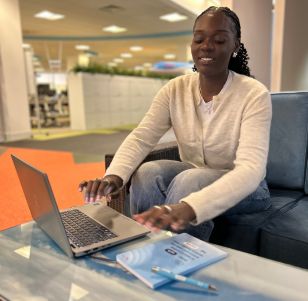A TUI colleague sits in an open office space smiling looking at her laptop