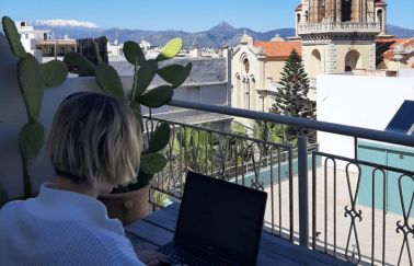 A remote working TUI colleague sits at her laptop on a balcony looking out to a Spanish view