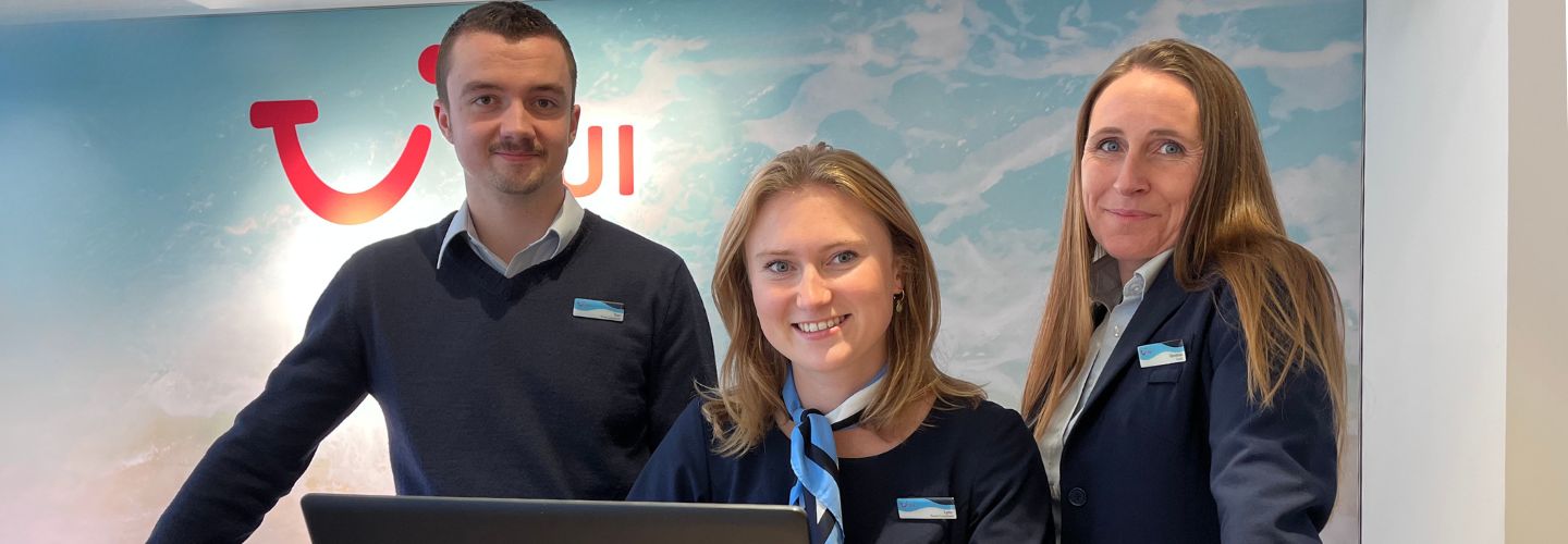 A group of three Travel Agents behind a laptop smiling at the camera