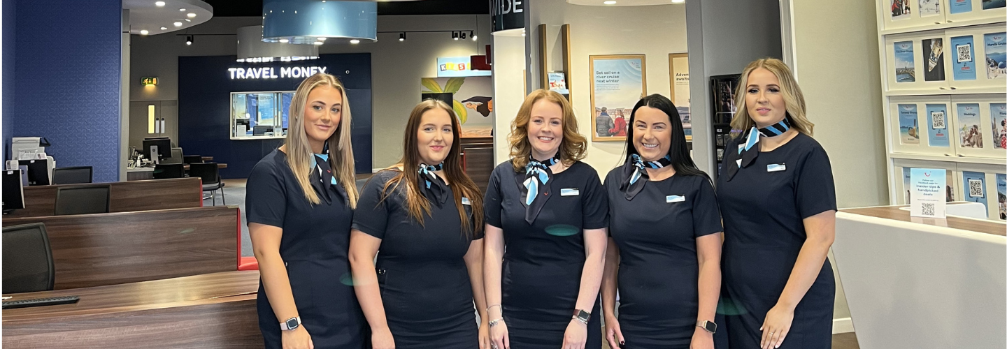 Five retail employees in front of the store smiling at the camera
